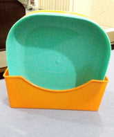 A plastic pet scoop with a bright orange base and a mint green interior, shown on a light gray surface.