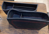 Two black car storage bins with red stitching on a wooden surface.