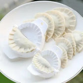 Dumpling maker with uncooked dumplings on a white plate