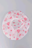 A white silicone shower cap with a pink lip and heart pattern, photographed from directly above on a light gray background.