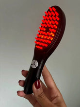 Black hairbrush with red bristles held by a hand against a neutral background