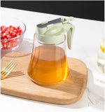 Glass container with a green lid on a wooden cutting board, surrounded by pomegranate seeds and a gold fork.