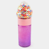 A novelty bottle shaped like a gumball machine, with a glittery purple-to-pink gradient body, a light pink collar, and a clear top filled with multicolored gumball-like beads, shown on a light gray background.
