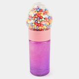 A novelty bottle shaped like a gumball machine, with a glittery purple-to-pink gradient body, a light pink collar, and a clear top filled with multicolored gumball-like beads, shown on a light gray background.