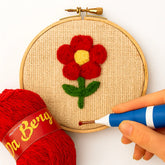 Embroidery hoop with a red flower design, red yarn, and a needle on a white background
