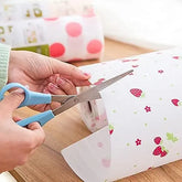 Person cutting patterned paper with blue-handled scissors on a wooden surface