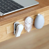 Desk with laptop, earbuds, and a white cable management product on a wooden surface.