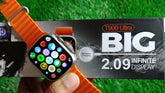 Smartwatch with orange band held in front of its packaging on a grass background