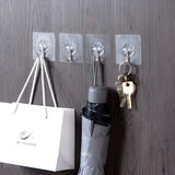 Clear hooks attached to a wooden wall with a bag, umbrella, and keys hanging from them.