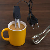 An electric coffee maker insert with a black power cord and metal heating element shown next to a yellow mug filled with coffee on a dark wooden surface.