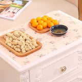 Nuts on a wooden tray with oranges and a small bowl on a floral-patterned surface.