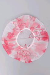 A circular white shower cap with a pink floral pattern, laid flat on a light gray background.