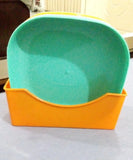 A plastic pet scoop with a bright orange base and a mint green interior, shown on a light gray surface.
