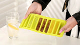 Person holding a yellow silicone ice cube tray with food items on a white surface.