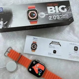 Smartwatch with orange band on a gray surface next to its packaging
