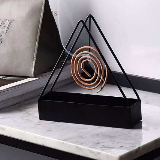 Triangular black metal holder with a coiled incense stick on a marble surface.