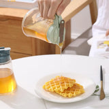 Person pouring syrup from a clear container onto waffles on a white plate.