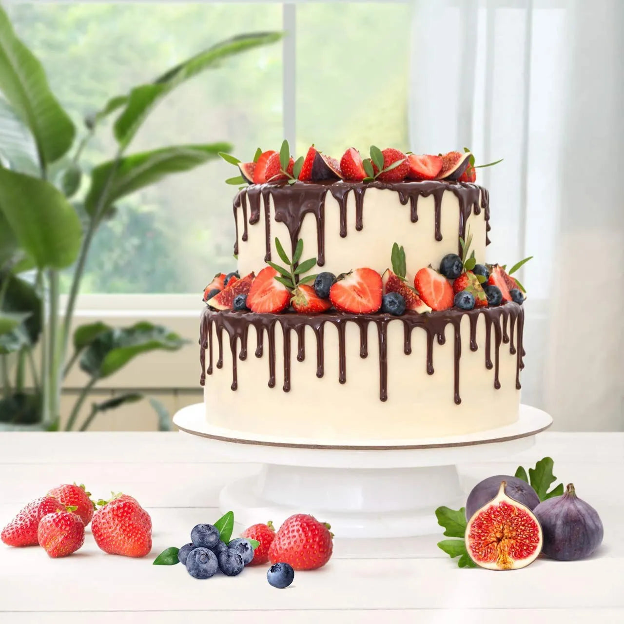 Two-tiered cake with chocolate drizzle and fresh fruits on a white surface with a plant in the background.