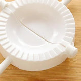 A white plastic dumpling wrapper press mold with a scalloped rim, shown on a light wood surface.