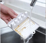White soap dish with soap bars being rinsed under running water in a sink.