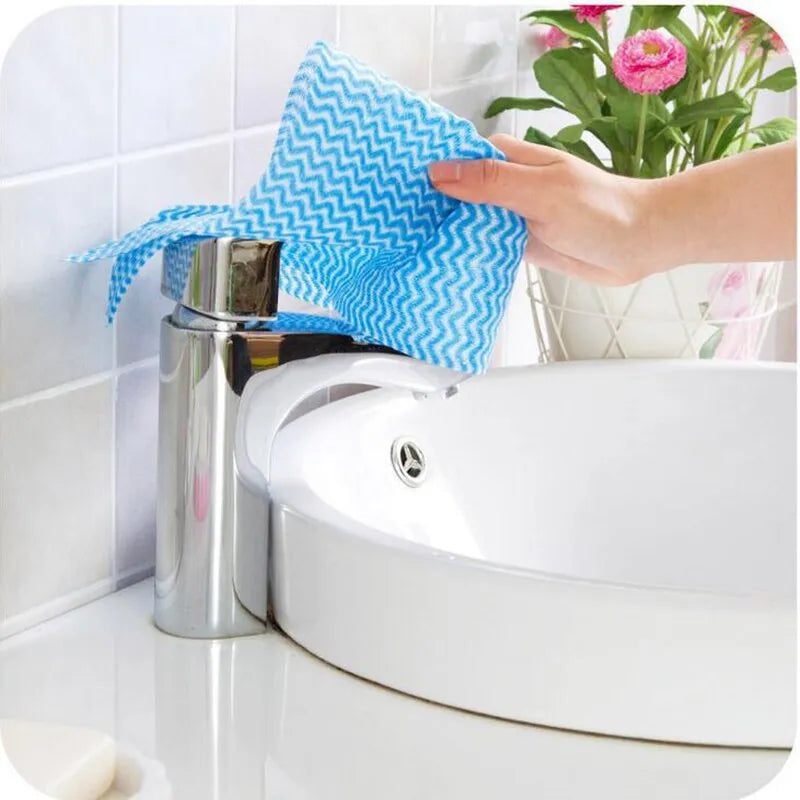 Hand cleaning a faucet with a blue chevron patterned cloth, with a white sink and tiled wall in the background.