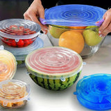 Silicone food covers on various fruits and vegetables with hands holding a bowl.