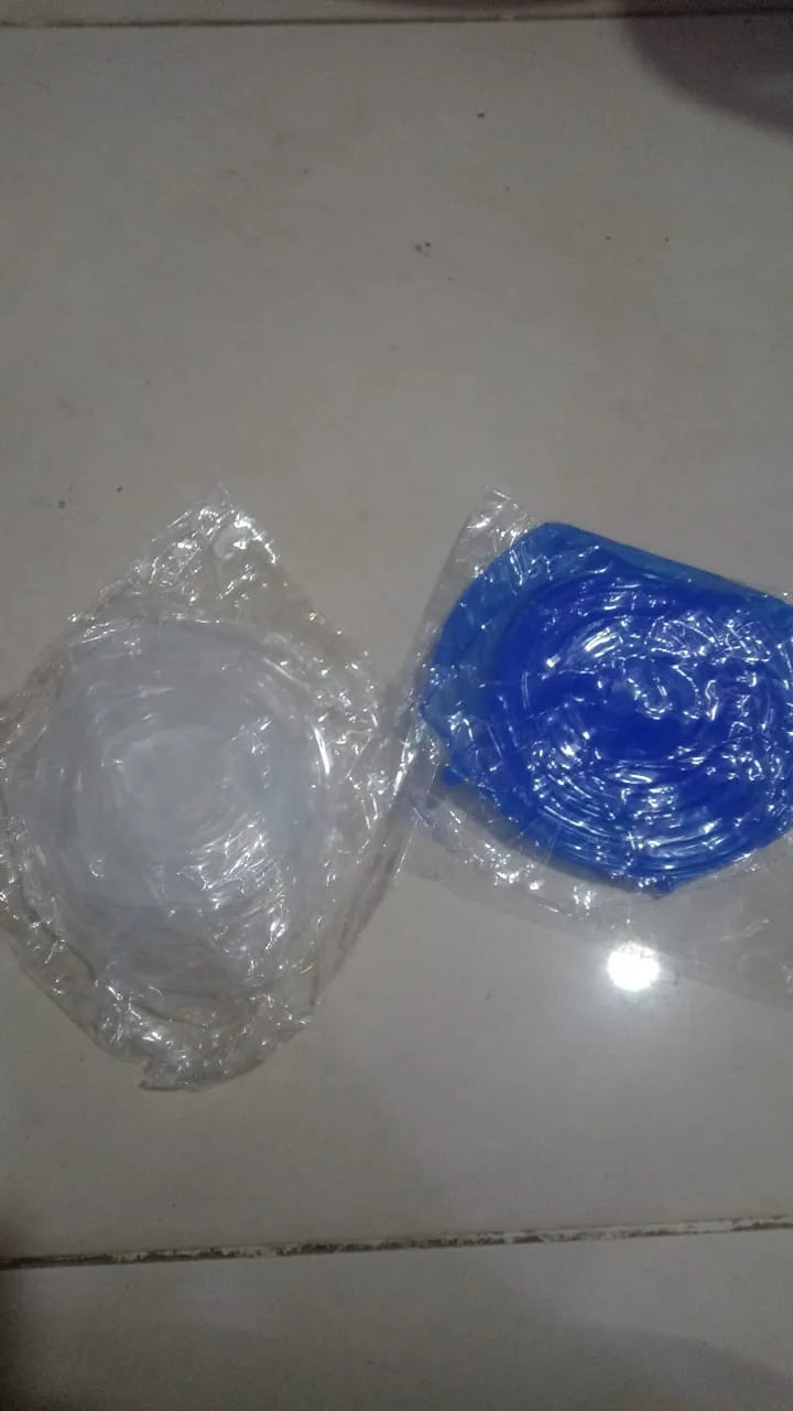 Two small plastic-wrapped items on a light floor: a clear round item on the left and a blue square item on the right, both sealed in transparent plastic.
