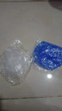 Two small plastic-wrapped items on a light floor: a clear round item on the left and a blue square item on the right, both sealed in transparent plastic.