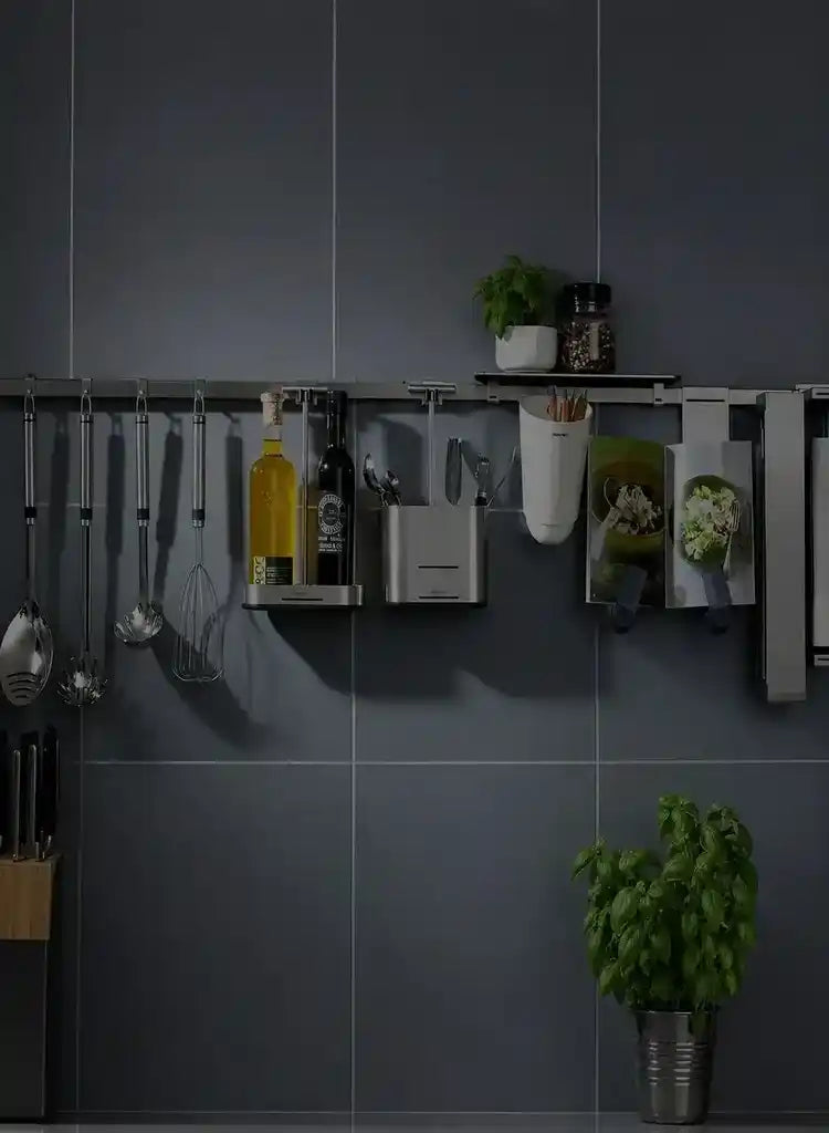 Wall-mounted stainless steel kitchen utensil organizer rail on dark grey tiled wall.
