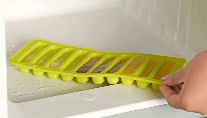 Yellow ice cube tray being placed into a freezer.