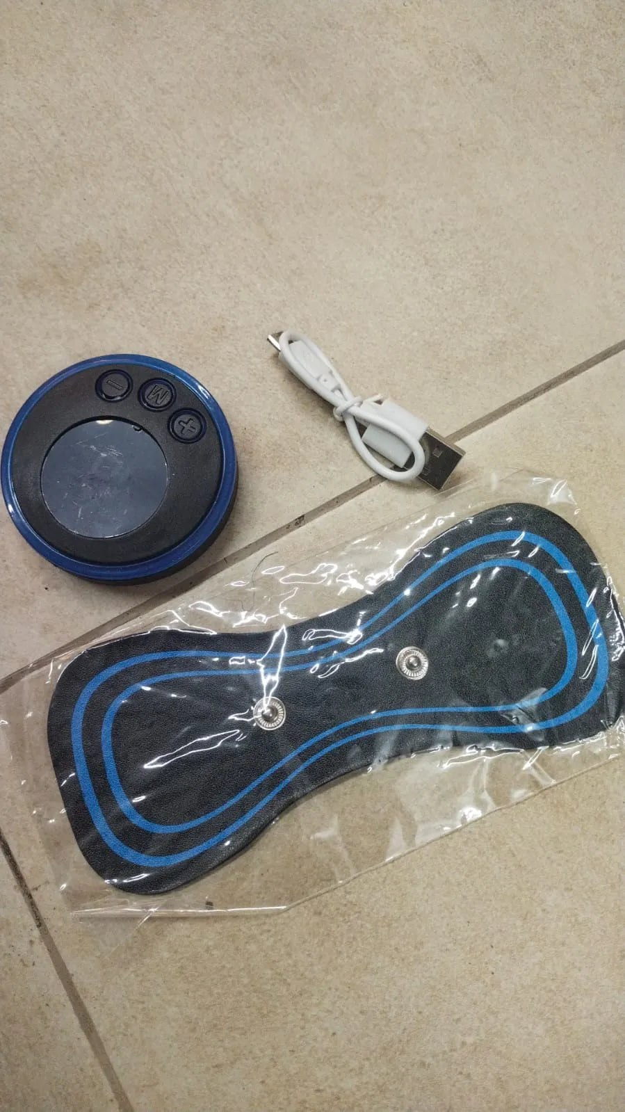 Black and blue electronic device with buttons on a beige tiled floor.