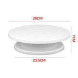 White plastic cake turntable shown with red dimension labels indicating 28 cm top diameter, 23.5 cm bottom diameter, and 7 cm height on a light gray background.