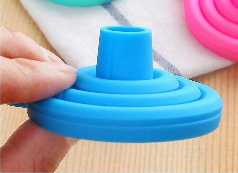 Blue silicone cup holder being held by a hand on a wooden surface with other colorful holders in the background.