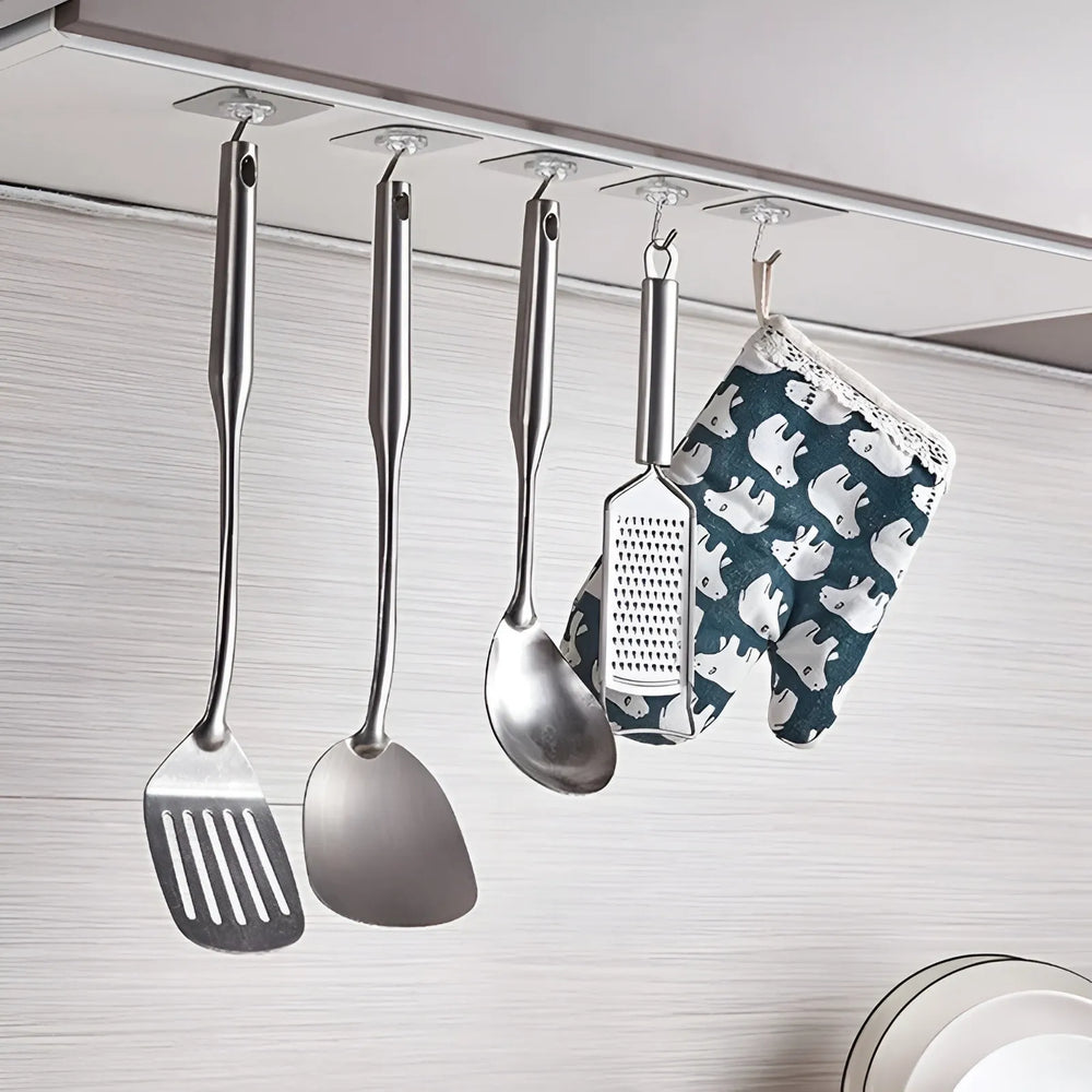 A set of stainless steel kitchen utensils, including a spatula, spoon, ladle, and grater, hanging from a metal rod on a wall, alongside a blue and white patterned oven mitt.