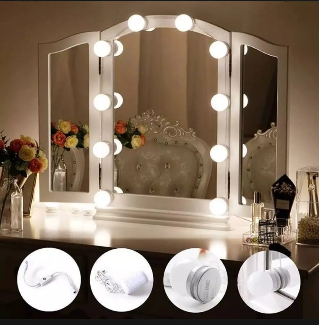 Tri-fold vanity mirror with lights on a desk, surrounded by decorative items.
