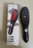 Black hairbrush with red bristles next to its packaging on a light surface