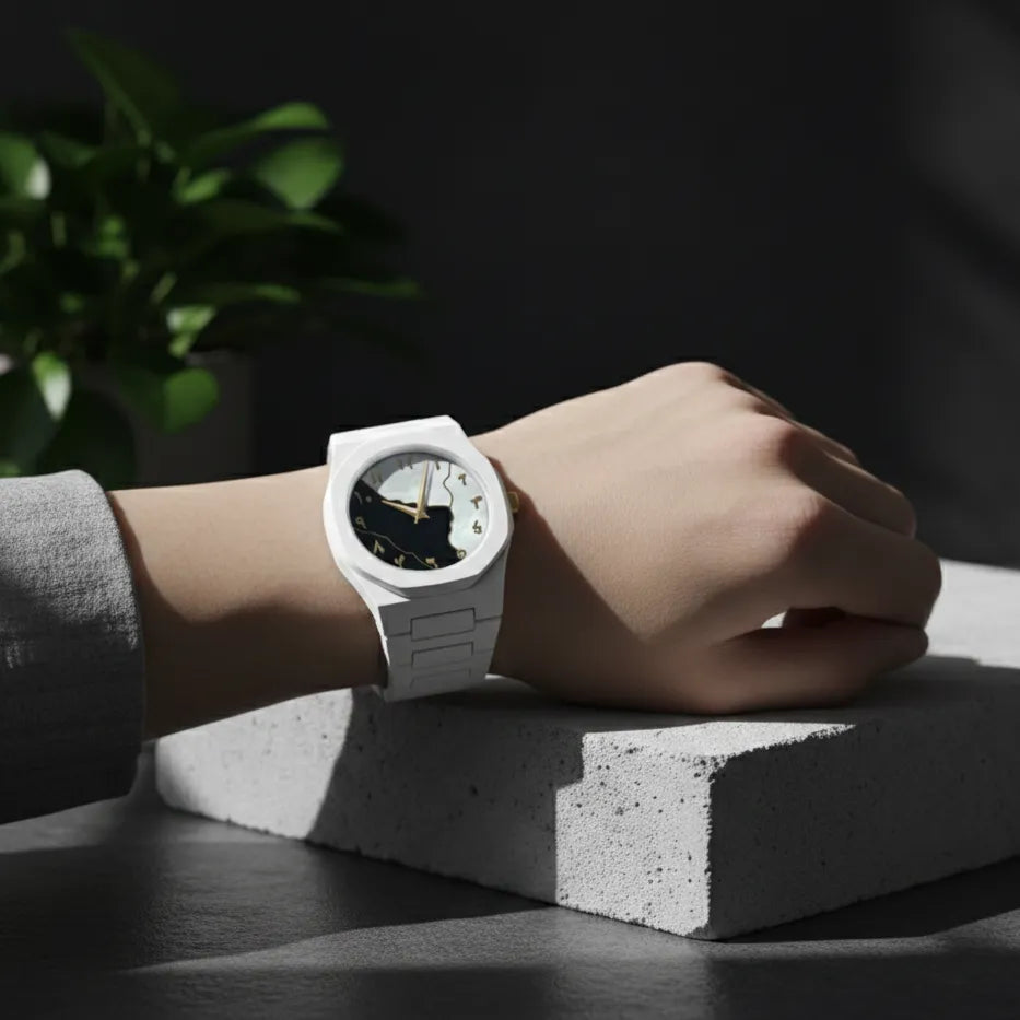 Person wearing a white watch with a black face on a dark surface, plant in the background