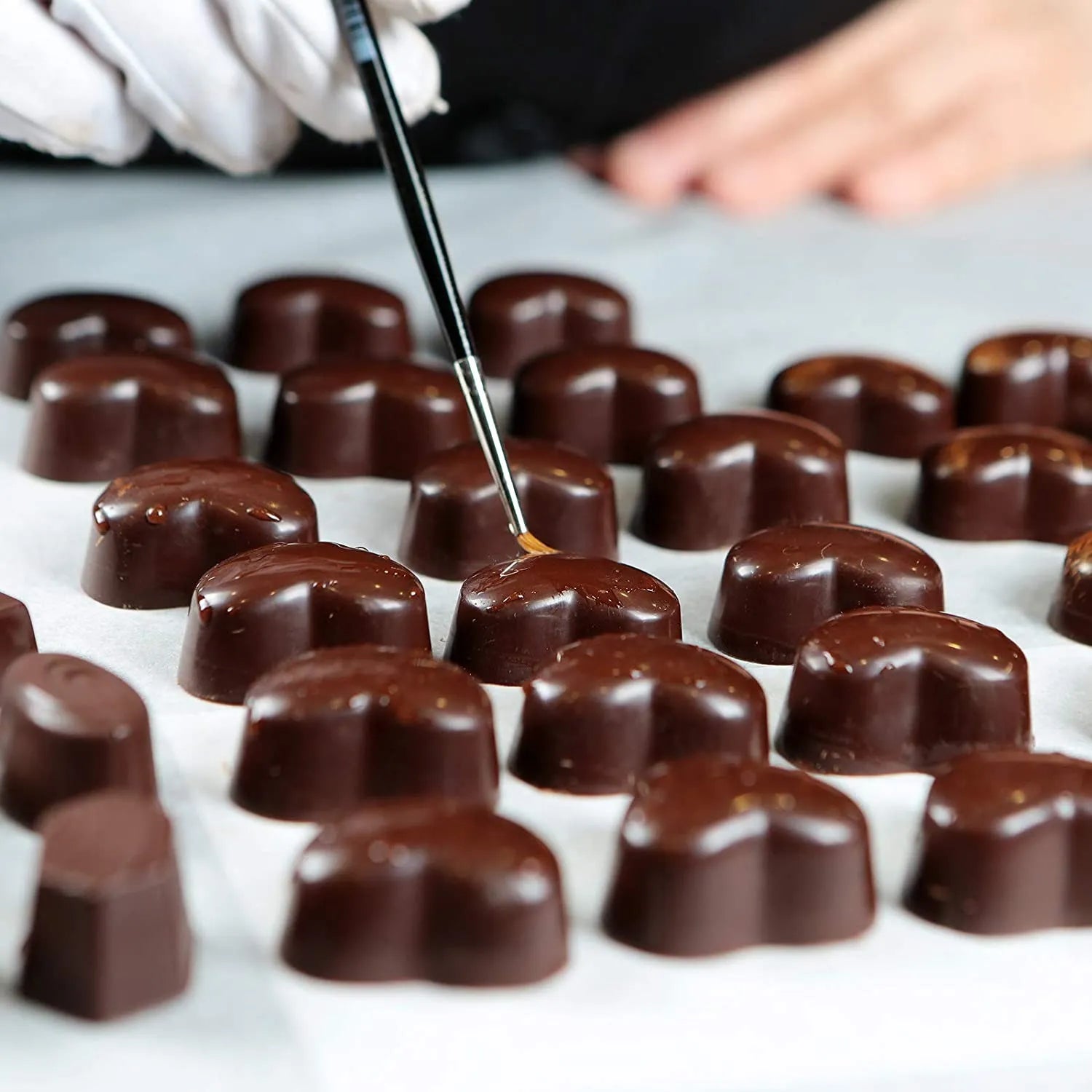 Chocolate truffles being decorated with a tool on a white surface.