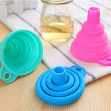 Set of colorful silicone funnels on a wooden surface with a glass of liquid in the background.