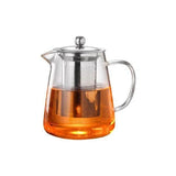Clear glass teapot with metal lid and handle filled with orange liquid on a white background