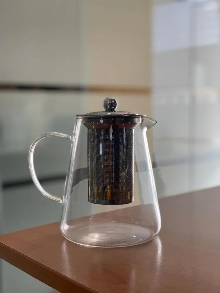 Clear glass teapot with metal lid on a wooden surface