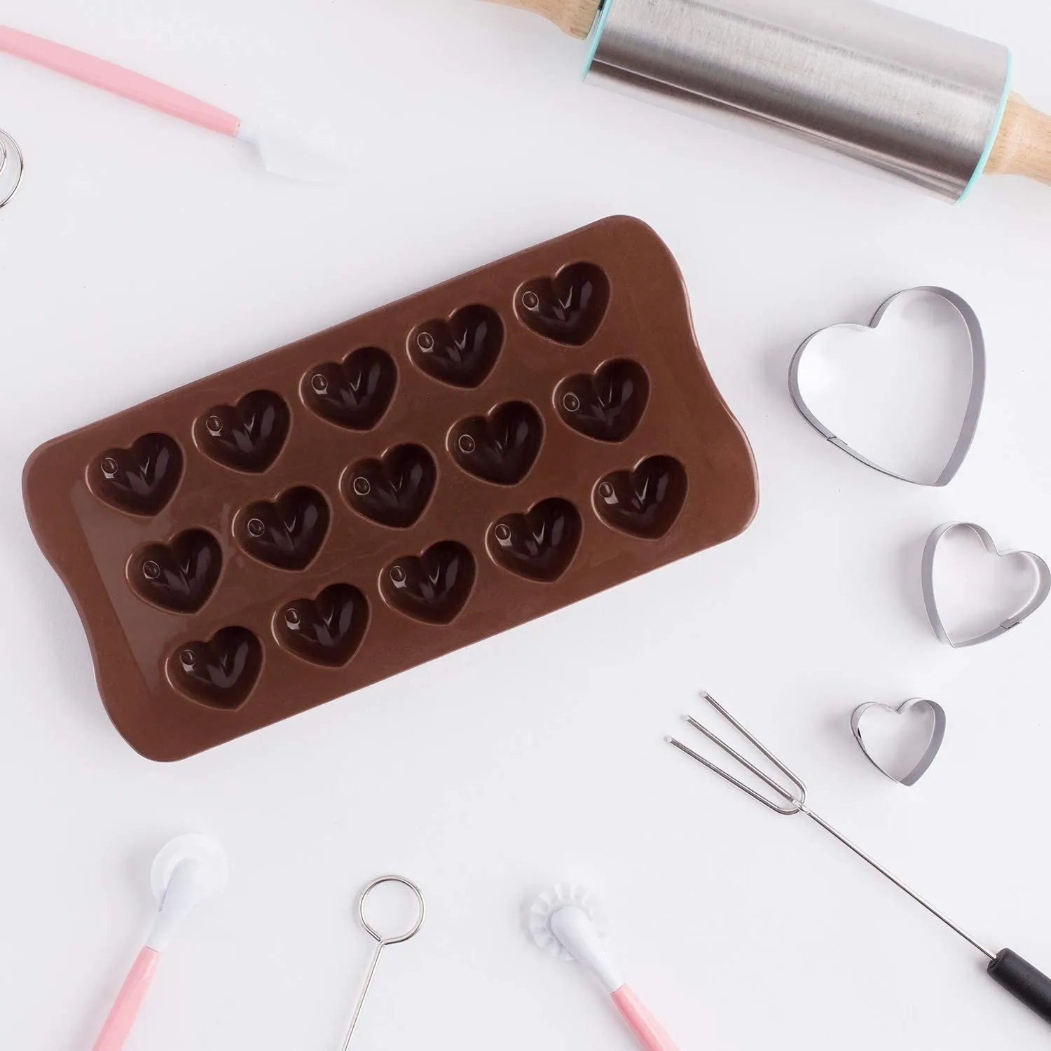 Chocolate mold with heart shapes on a white surface with baking tools.