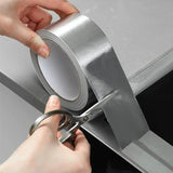 Person cutting a roll of silver tape with scissors on a neutral background