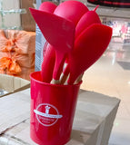 Set of red silicone kitchen utensils in a red holder on a table.