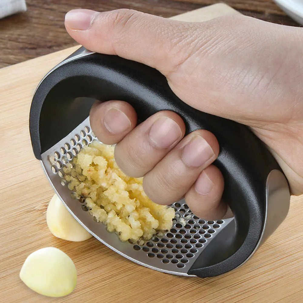 Hand using a garlic press on a wooden surface with crushed garlic visible.