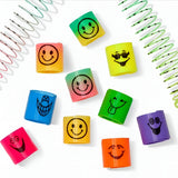 A set of colorful plastic twist-up wristbands with black cartoon smiley face designs, arranged on a white background with decorative spiral spring props.
