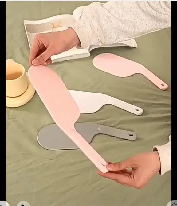 Person holding a pink spatula on a green surface with other spatulas and a cup.