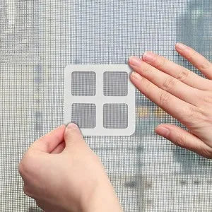 A person's hands demonstrating a white square window screen mesh cover with four quadrants, shown being applied to a window screen.
