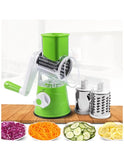 Green manual vegetable spiralizer with attached blades on a wooden surface, surrounded by sliced vegetables.