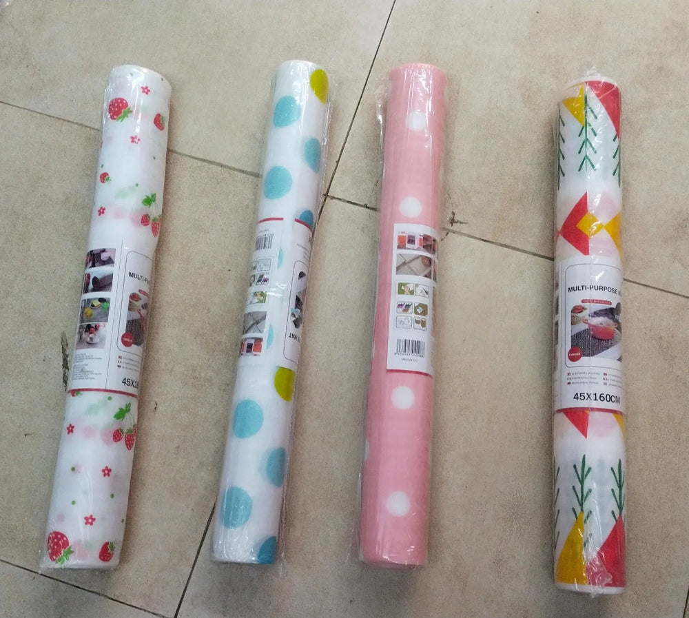 Four rolls of kitchen wrapping paper laid out on a beige tiled floor. The rolls feature different patterns: strawberry and daisy prints, blue polka dots, white polka dots, and a red, yellow, and green geometric pattern.